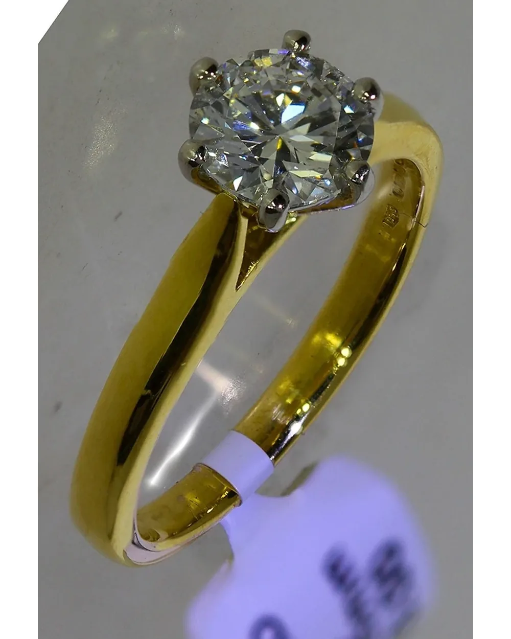 Gold solitaire ring as shot, with a price tag and grey background